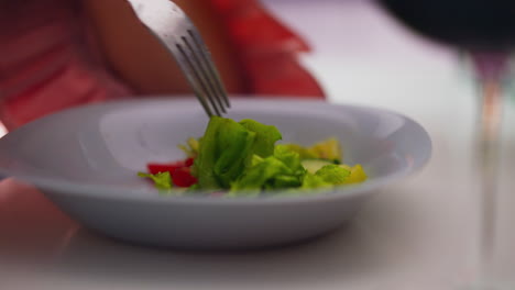 recogiendo ensalada con tenedor de plata en el plato en la mesa blanca