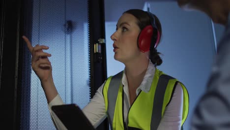 diverse female and male it technicians wearing headphones using tablet checking computer server