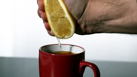 man squeezing lemon into red mug