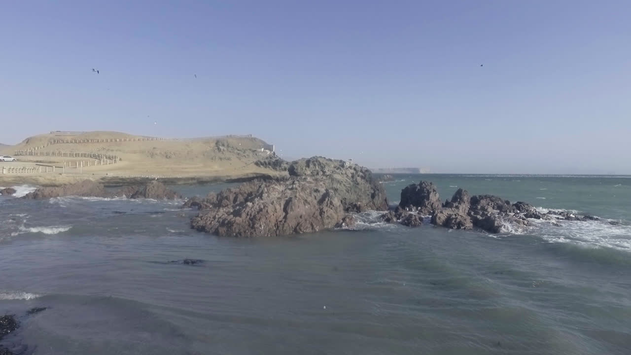 Beautiful drone shot of the shoreline of a beach as the waves crash against the stones during the day