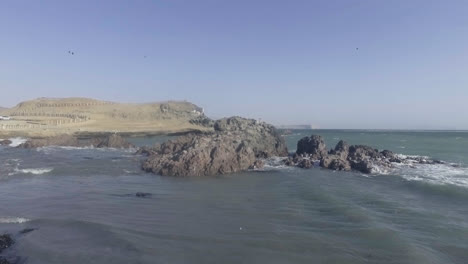 Beautiful-drone-shot-of-the-shoreline-of-a-beach-as-the-waves-crash-against-the-stones-during-the-day