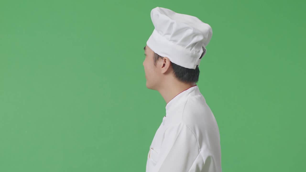 Vista laterale di uno chef asiatico che cammina e saluta con la mano in uno studio con sfondo a schermo verde