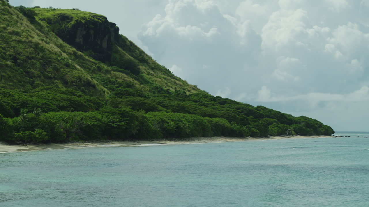 Tropical island coastline with forested slopes and turquoise shallows from boat