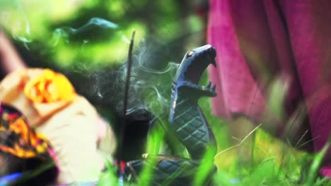 Incense-burning-over-ceremonial-cobra-shaped-incense-holder-in-outdoor-scene-with-grass-and-fabric-in-foreground-and-background