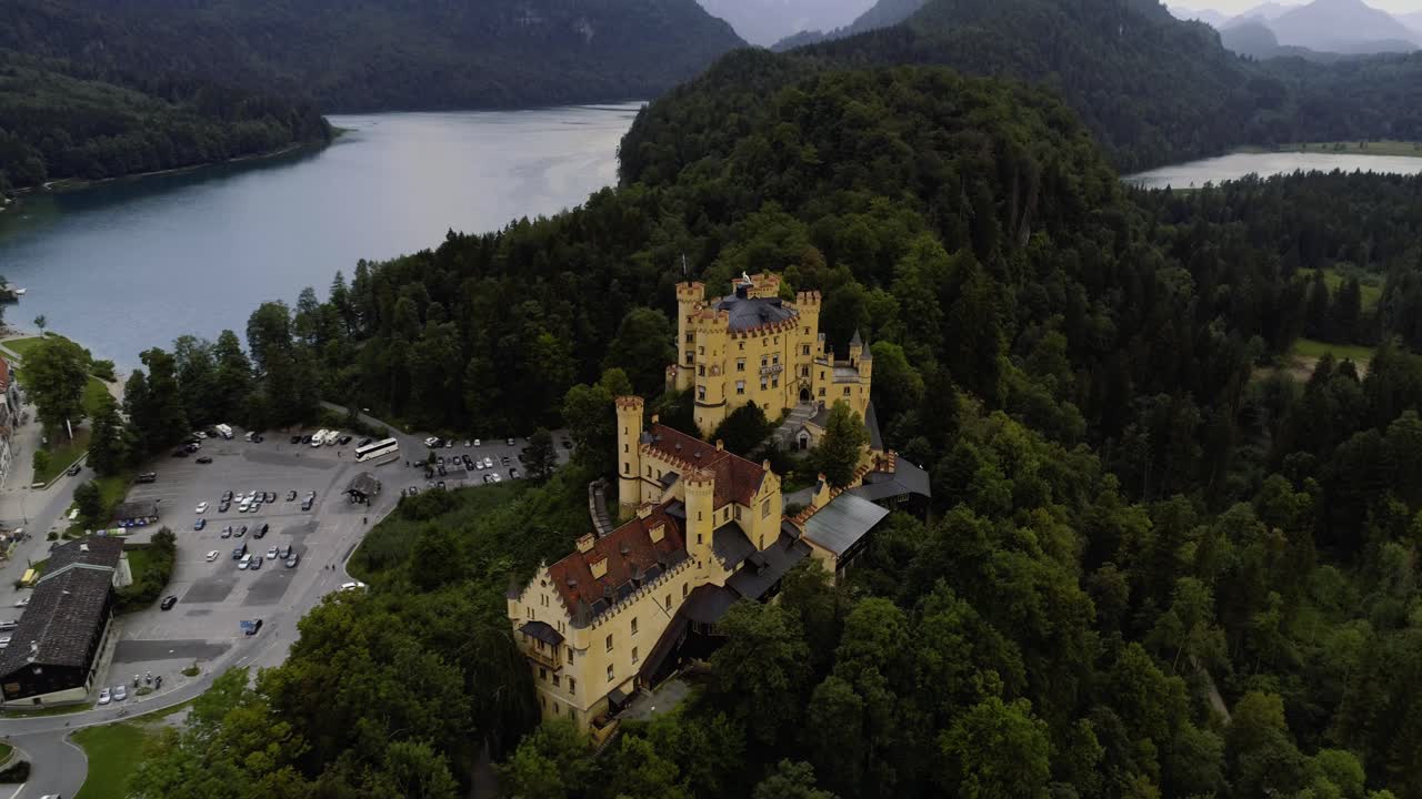 Volando all'indietro dal castello di Hohenschwangau, rivelando lo scenario delle montagne alpine e del lago Alpsee.