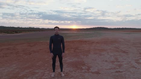 male model with dark hair, wearing wetsuit, stood facing camera in austrailan outback desert