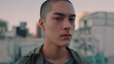 portrait attractive young mixed race man with shaved hair on rooftop at sunset wearing piercings looking confident in urban city background