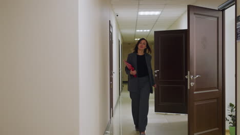 businesswoman walking through office corridor holding documents in formal attire, approaching open office doors, professional environment, modern workplace, corporate life, and productivity