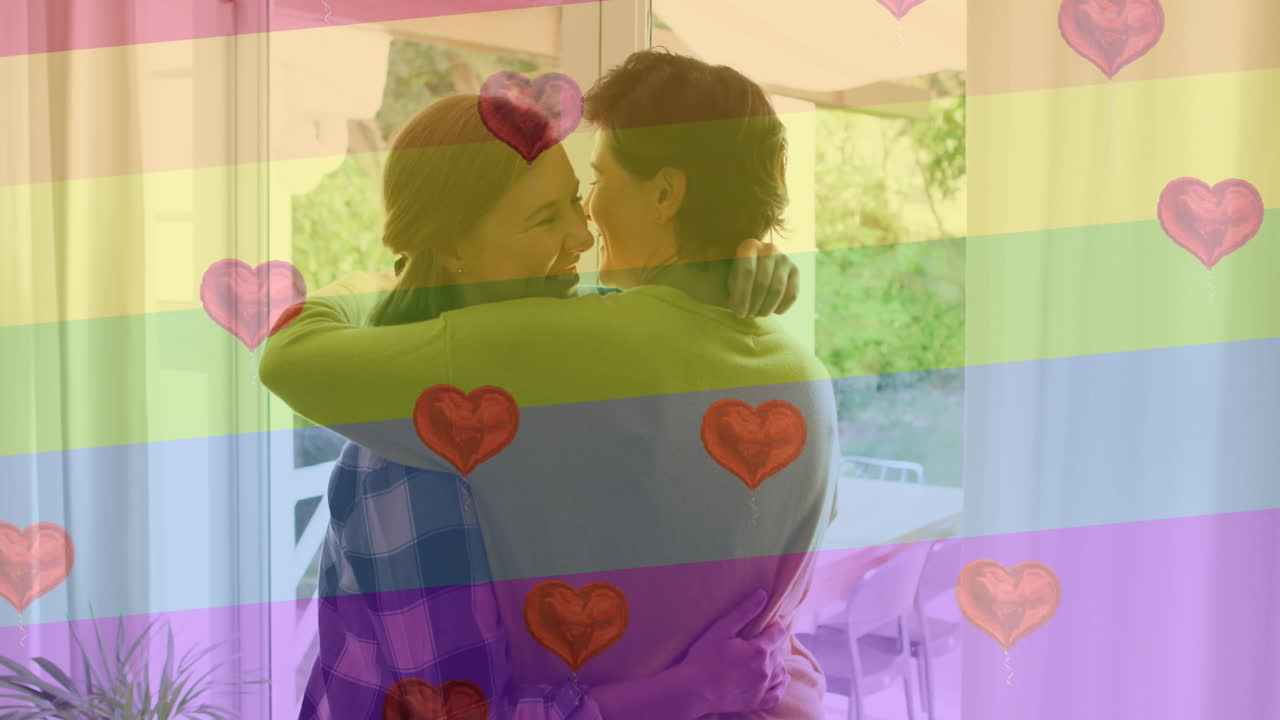 animación de emojis de corazón y bandera del arco iris sobre una pareja de mujeres caucásicas abrazándose