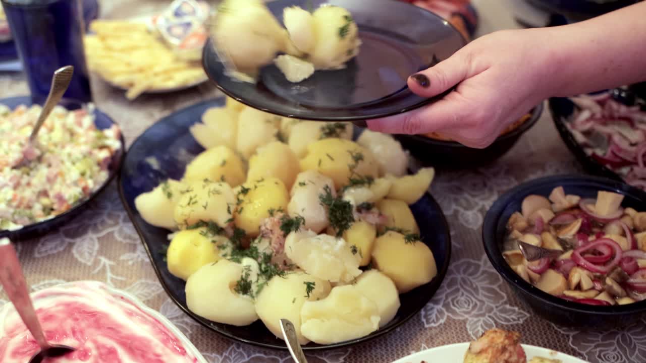 una mujer pone patatas hervidas en un plato en la mesa festiva. muchos platos en la mesa, caseros