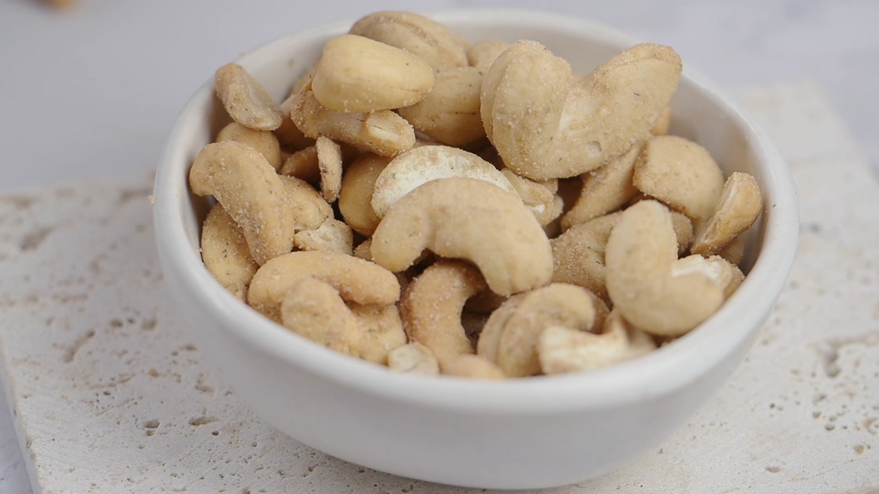 Close-up of Healthy Cashews Pouring into a White Bowl