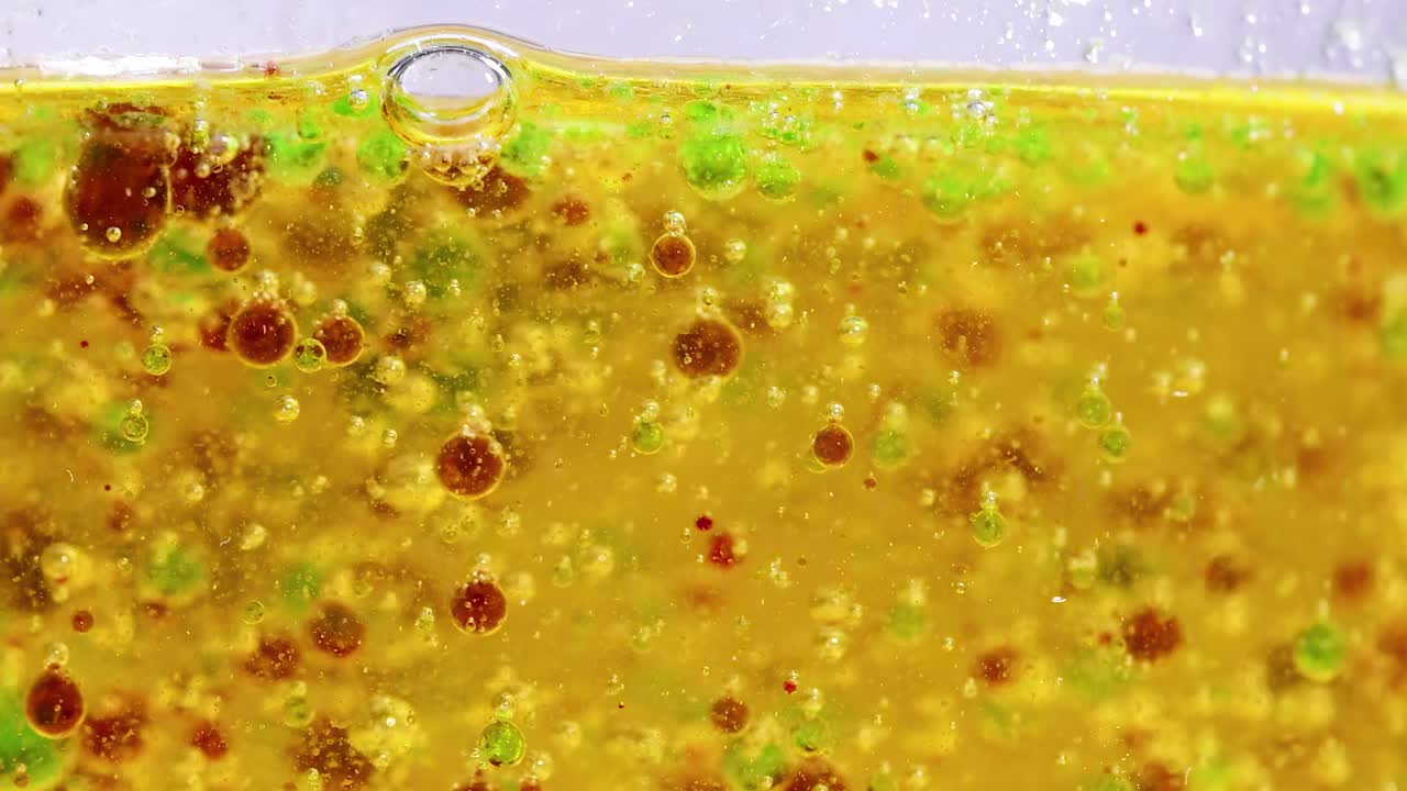 Close-up of colorful droplets floating in a golden liquid, showcasing dynamic movement and interaction.