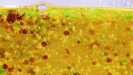close-up of colorful droplets floating in a golden liquid, showcasing dynamic movement and interaction.