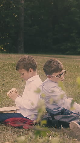 schoolboys wearing uniform sit near little blond girl with book in hands on school yard grass close view slow motion