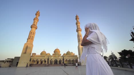puesta de sol, amanecer vista de la mezquita de el mina con mujer turista en largo vestido blanco y hijab disfrutando de la vista de la mesquita