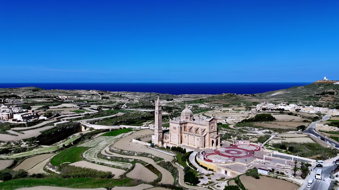 Breathtaking high angle aerial view of Ta Pinu National Shrine in Gozo Malta during a golden summer afternoon featuring neo-Romanesque limestone architecture and the iconic bell tower under blue sky