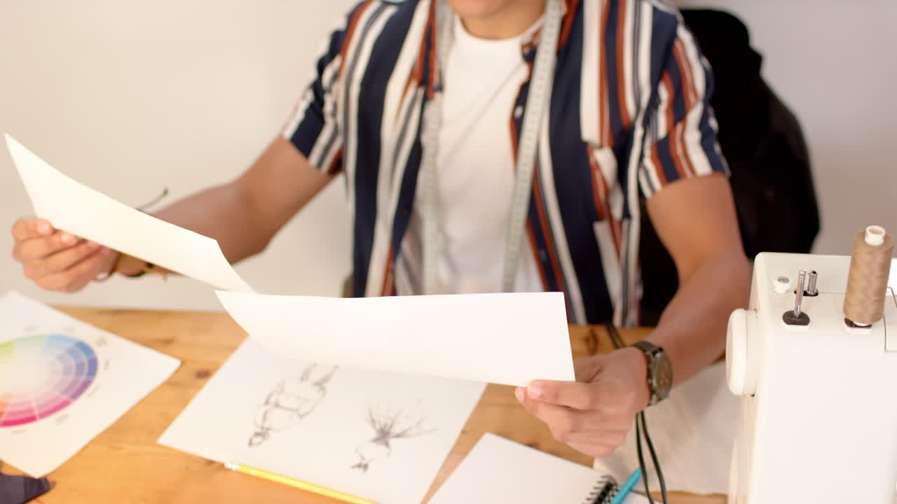 Biracial male fashion designer looking at sketched designs in studio, slow motion