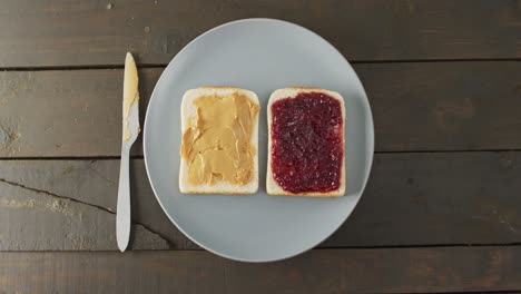 close up view of peanut butter and jelly sandwich in a plate with butter knife on wooden surface