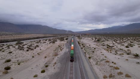 aerial drone footage of cargo train disappearing in the palm springs desert with wind farms in the background, steady shot