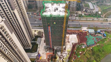 aerial view of a construction site on the outskirts of chongqing, china, showing a tall residential building under construction. the site is surrounded by scaffolding, machinery, and ongoing work.