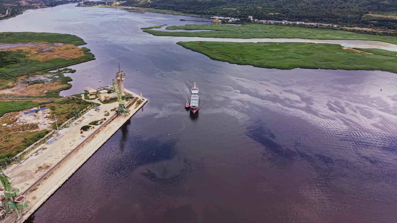 Nave da carico naviga lungo un fiume vicino a un paesaggio verde e edifici