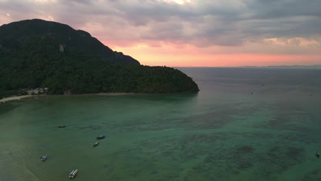 Spectacular-aerial-view-flight-of-a-tropical-island-at-sunset-cloudy-sky-with-boats-sailing-on-a-turquoise-sea