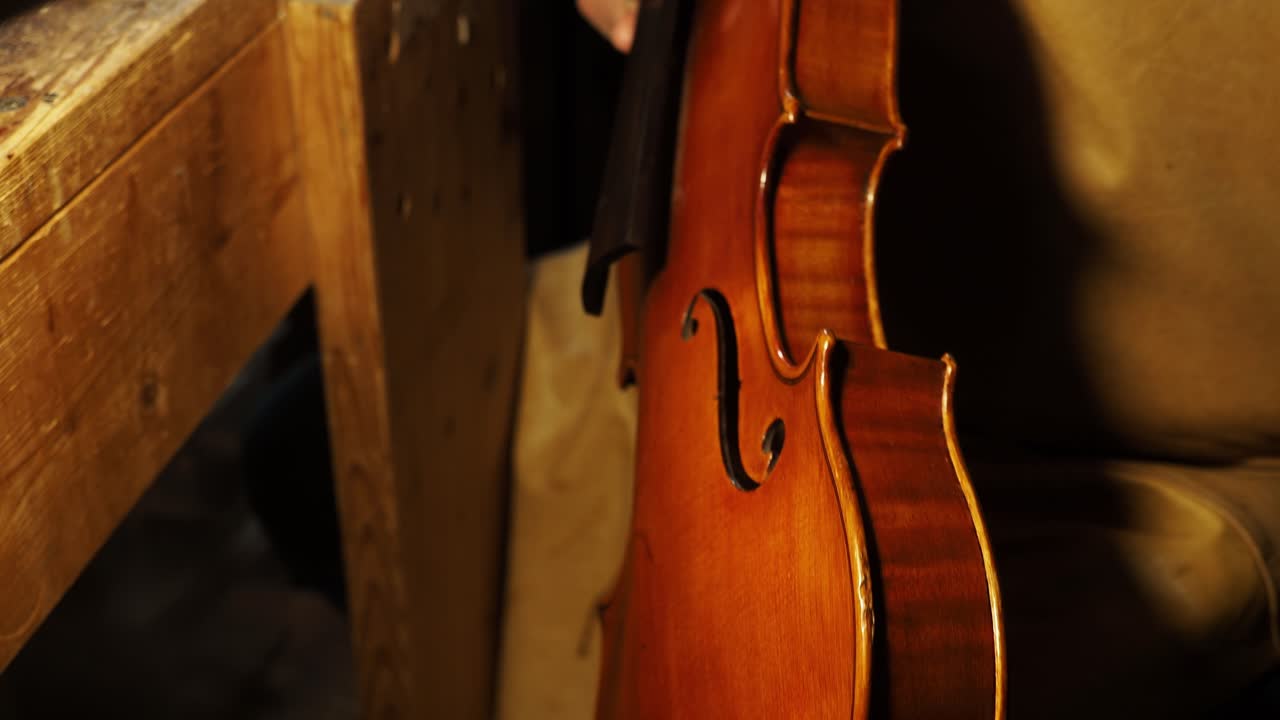 In the warm light of a traditional workshop, a luthier’s hands polish the finished body of a new violin, bringing out the radiant wood grain and rich, golden-brown Cremonese varnish