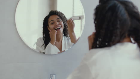 woman flossing her teeth in front of a mirror