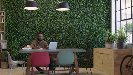 young african american businessman working late using laptop computer brainstorming planning strategy drinking coffee in trendy startup office