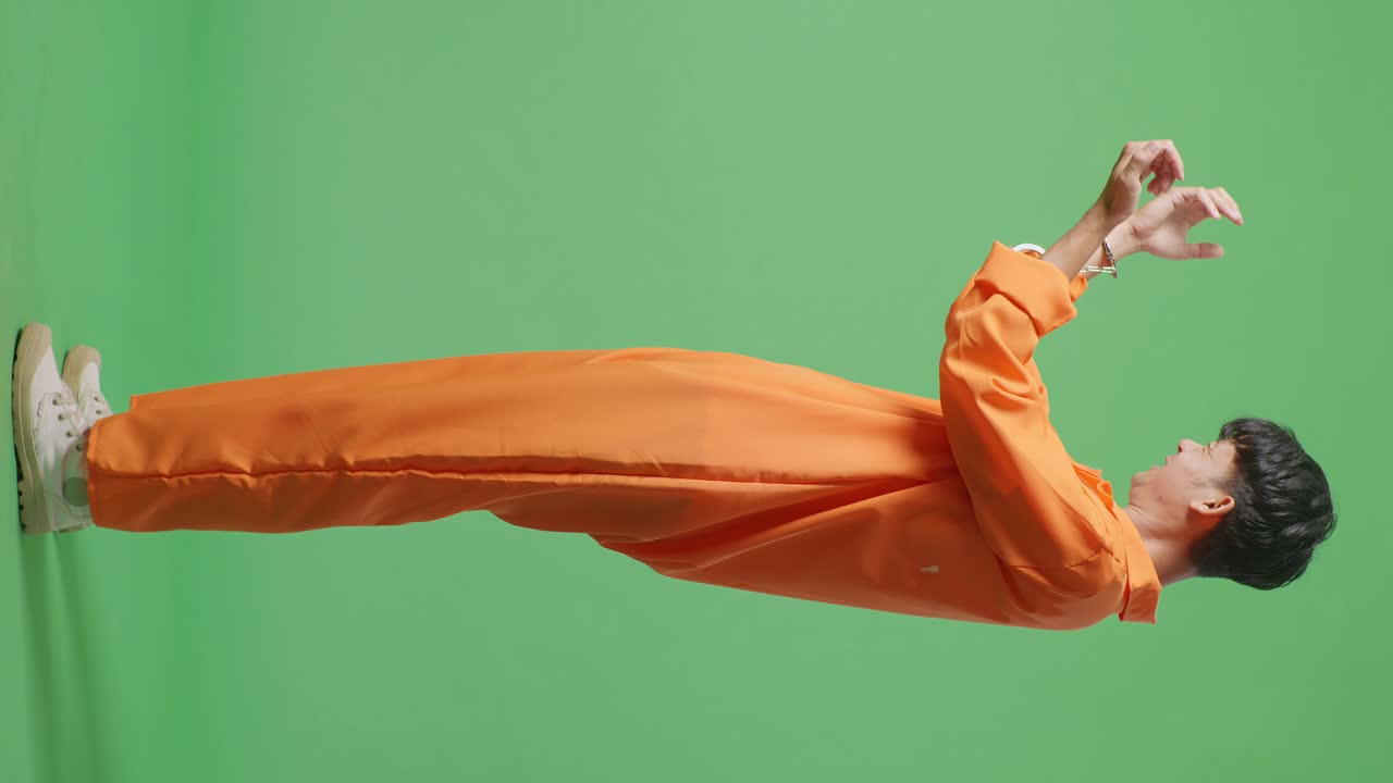 녹색 스크린 배경에 서서 축하하는 골을 비명을 지르며 손이 부러진 아시아 남성 수감자의 전체 몸 측면 뷰