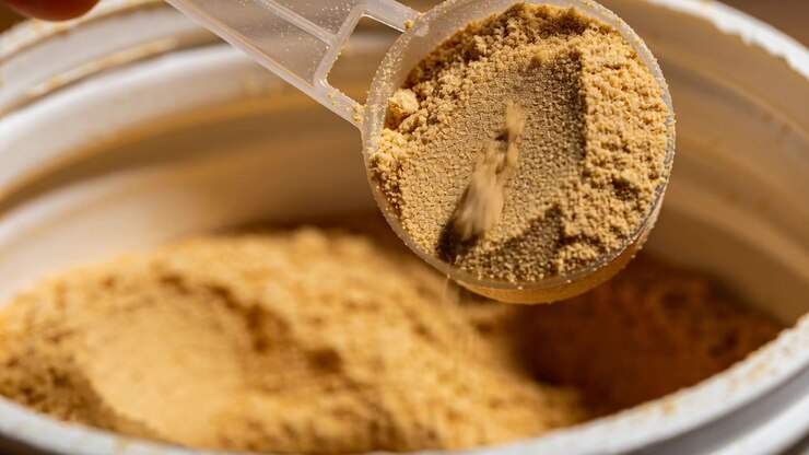 Tilting adult hand holding measuring scoop pouring beige powder into jar in kitchen for baking