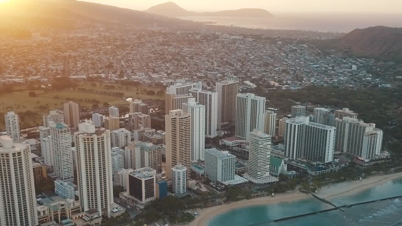 Drone aéreo panorâmico voando lentamente sobre o colorido horizonte de Honolulu durante o pôr do sol em Oahu, Havaí, com a Praia de Waikiki como um ponto de interesse especial