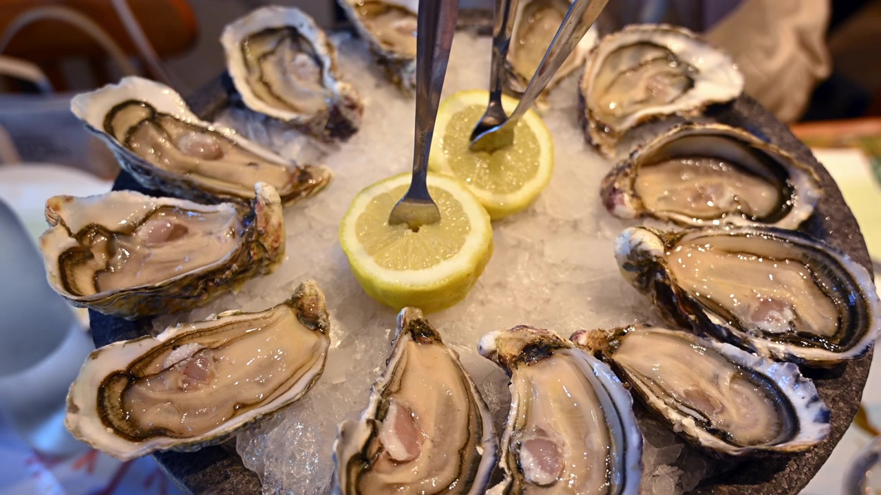 Ostriche fresche esposte su ghiaccio tritato con fette di limone in un ambiente da ristorante di pesce.