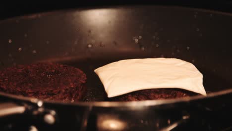 Vegan-PlantBased-Burgers-with-Cheese-being-Layered-on-Top-by-Hand-while-in-Hot-Pan