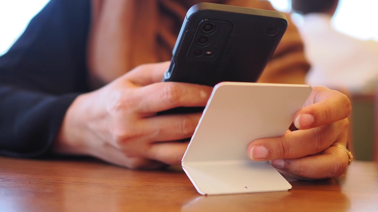 Primo piano di mani che tengono smartphone e carta per una transazione online.