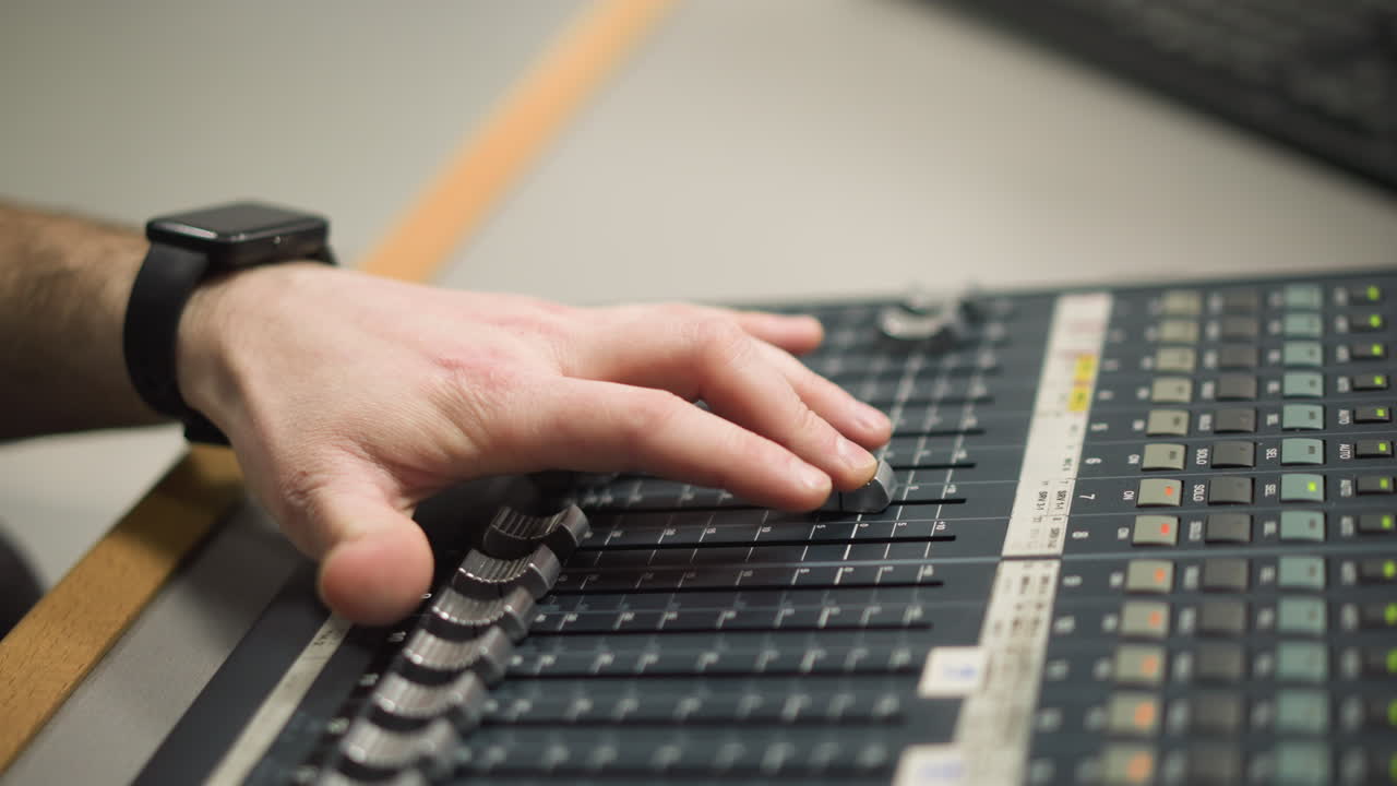 Close-up of hand adjusting fader on audio mixing console, controlling sound levels, professional broadcast studio or control room, focused on precise sound control and engineering
