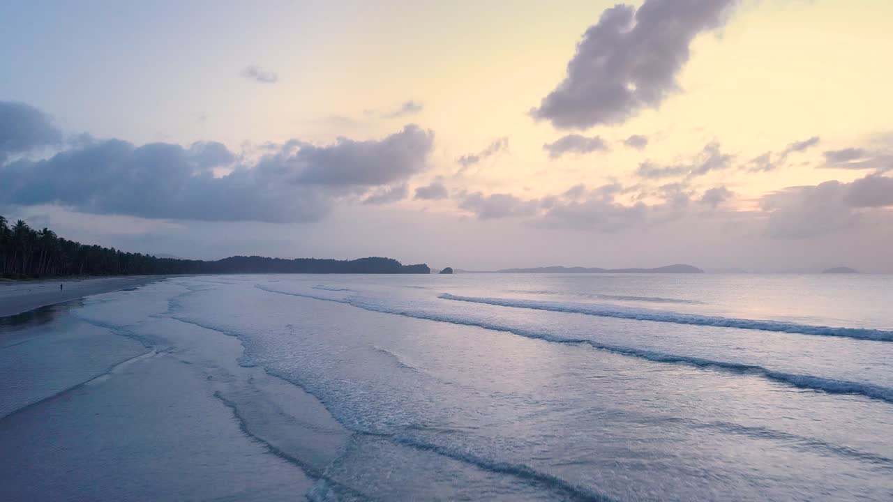 필리핀 팔라완의 일몰에 있는 긴 해변의 작은 잔잔한 파도 위로 항공 추적 촬영