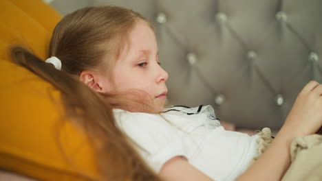 Thoughtful-little-girl-lies-on-sofa-with-soft-pillow-at-home