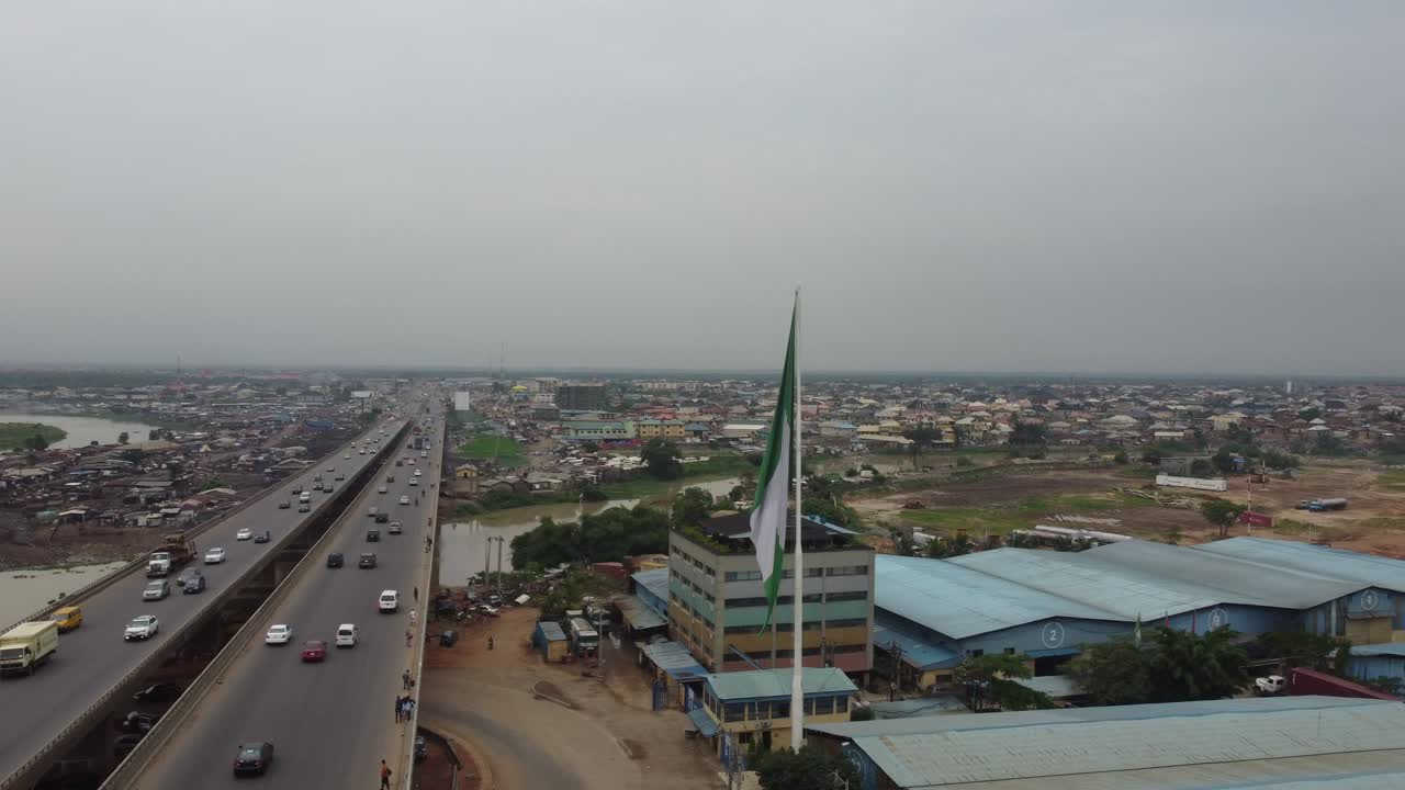 coches que se mueven rápidamente en el puente de una carretera suburbana con una bandera nigeriana frente a una industria