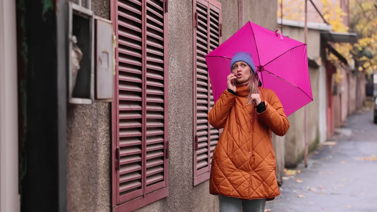Woman with pink umbrella talking on her phone on a rainy street