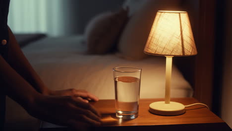 hand reaching for a glass of water on a nightstand