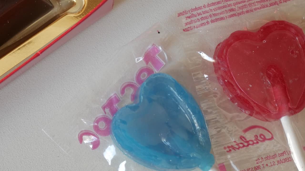Two heart-shaped lollipops, one red and one blue, wrapped in a clear package, for Valentine's Day