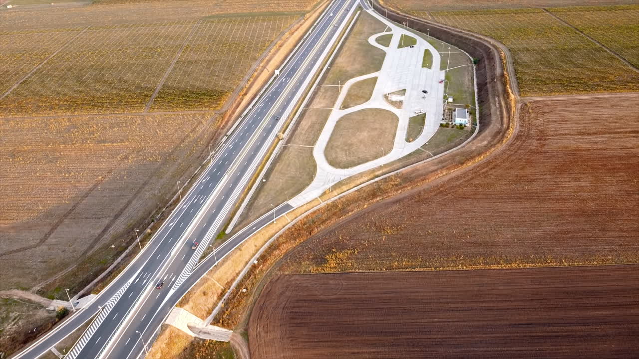 The Motorway of the Sun with moving cars and parking on the side of the road, fields around. View from the drone. Romania
