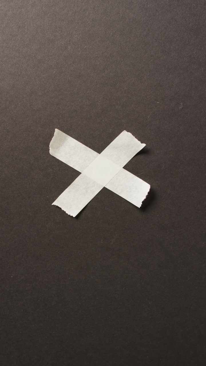 Video of close up of white paper tape forming cross on black background with copy space