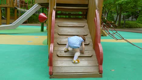 one-year-old toddler girl learnig to climb wooden ladder at playground in a park - mixed korean-ukrainian baby