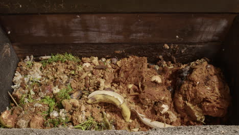 closeup slomo of household food waste dumped into wooden composting bin