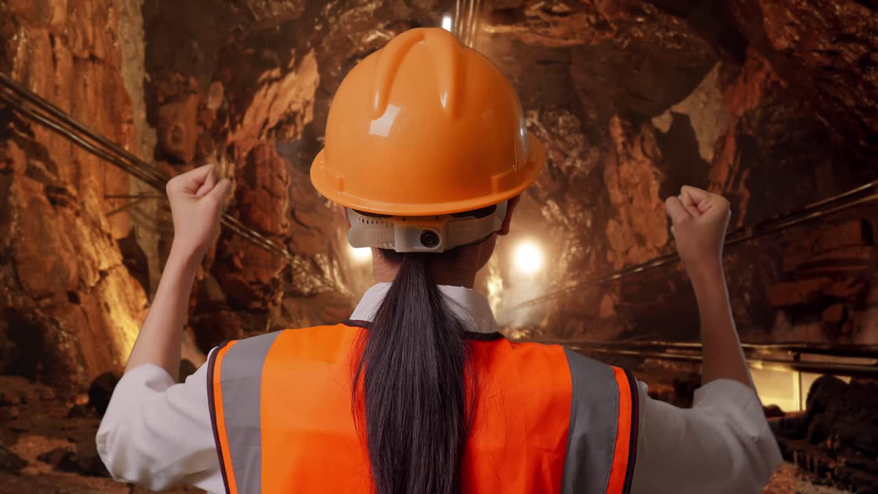 Close Up Back View Of A Female Engineer With Safety Helmet Raising Her Hands Celebrating While Working In Underground Mine Tunnel