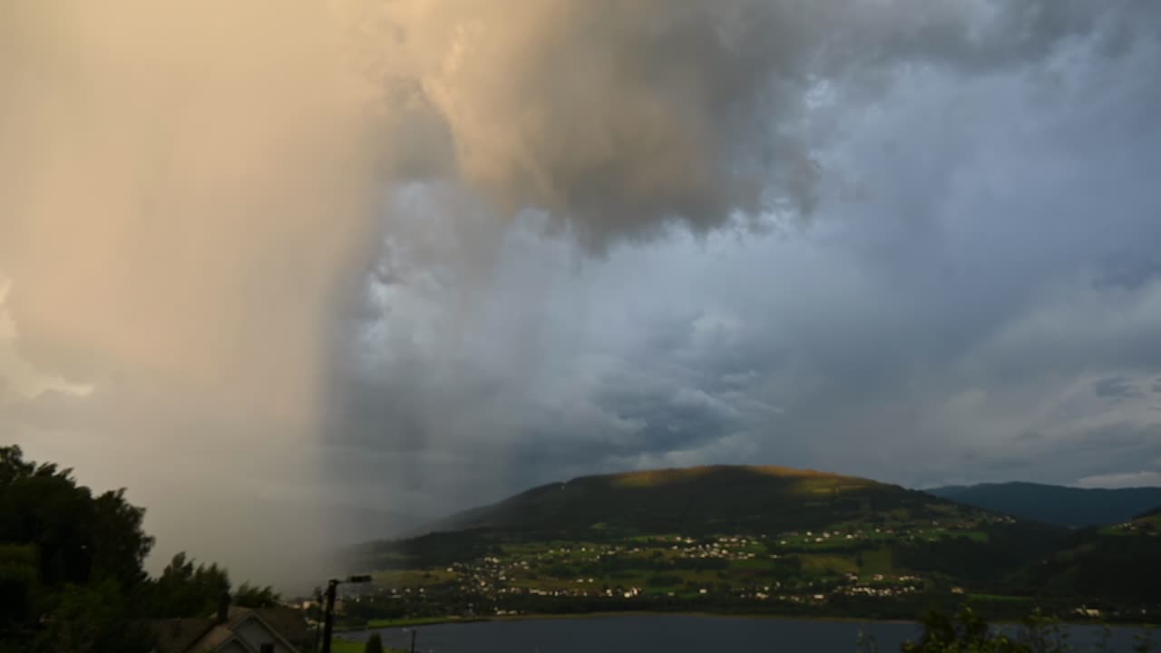 Branched lightning erupts behind Voss as low storm clouds hang over lake Vangsvatnet during summer thunderstorm