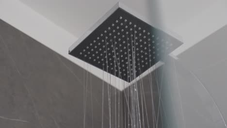 close-up of water flowing from modern square showerhead in contemporary bathroom setting