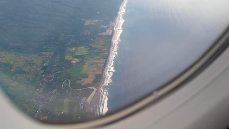 aerial view from airplane window of land, coastline, and ocean of indonesia flying into tropical island of bali